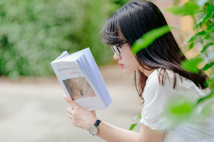 A woman reading a book outdoors, showcasing signs of intelligence.