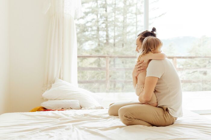 Parent and child sitting together on a bed by a window, showcasing signs of intelligence through affection and connection.