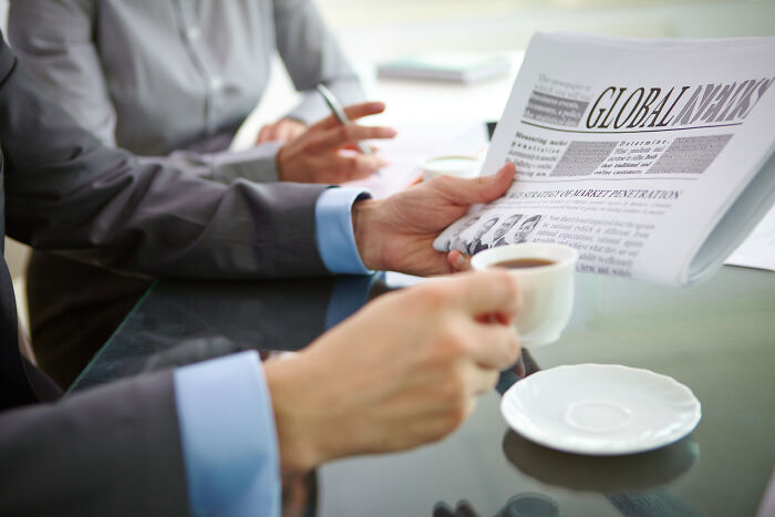 Business meeting with two people, one holding a cup and newspaper, discussing signs of intelligence.
