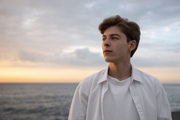 Young man in a white shirt by the ocean, contemplating signs of intelligence at sunset.