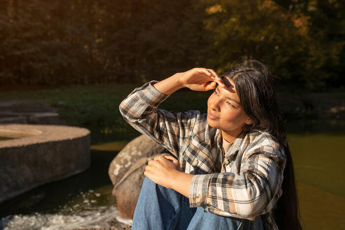 A woman in a plaid shirt sitting outdoors, gazing thoughtfully, highlighting signs of intelligence.