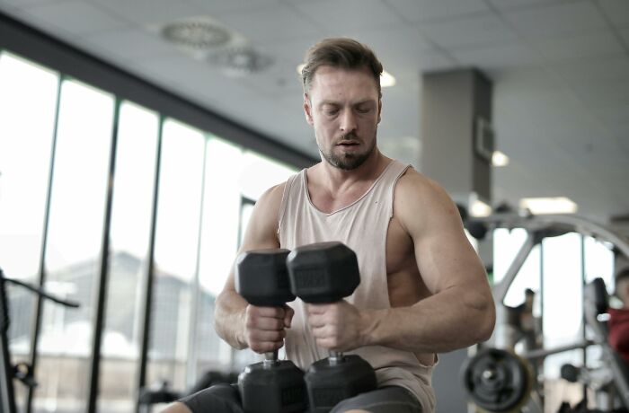 Man exercising with dumbbells in a gym, demonstrating signs of intelligence through physical discipline and dedication.