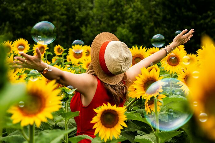 A woman in a sunflower field, arms raised, wearing a hat, symbolizing intelligence signs.