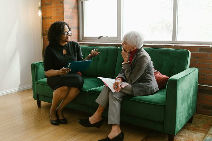 Two women sitting on a green couch having a conversation, illustrating signs of intelligence.