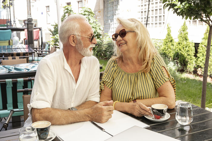 Older couple enjoying coffee at a cafe, discussing unaffordable expenses impacting the middle class.
