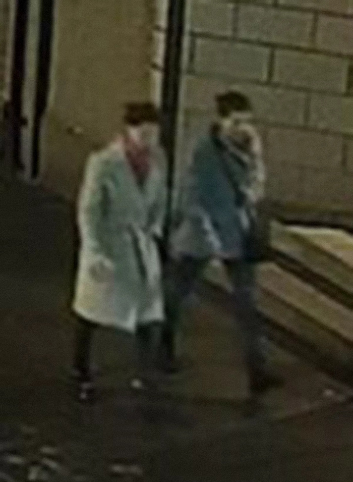 Two people walking beside a brick wall at night, linked to missing sisters case.
