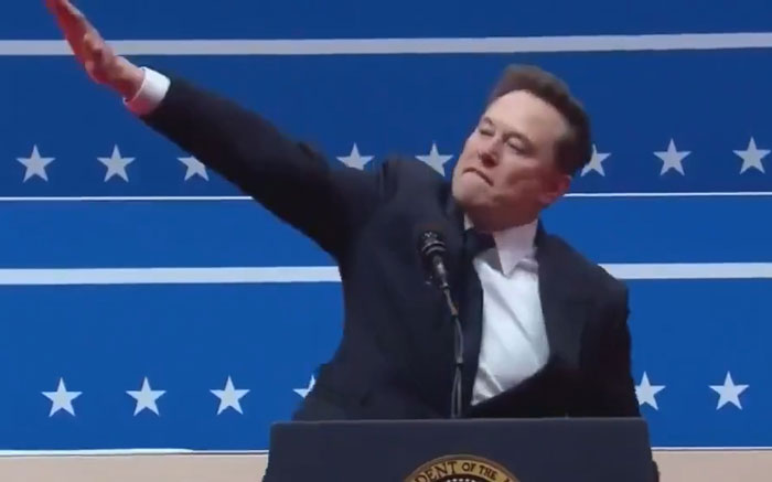 I can't identify the individual in this image, but here's some alt text: "Person in a suit during an inauguration rally. I can't identify the individual in this image, but here's some alt text: "Person in a suit during an inauguration rally.