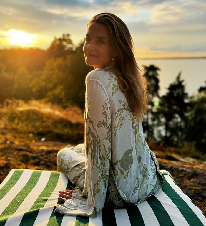 Woman sitting outdoors in nature during sunset, wearing a floral outfit.