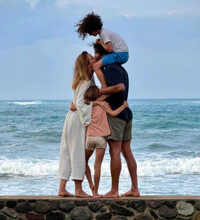 A family hugs by the ocean on a cloudy day, with waves in the background.