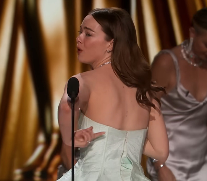 Emma Stone in a strapless dress on stage during an awkward moment at an awards show.