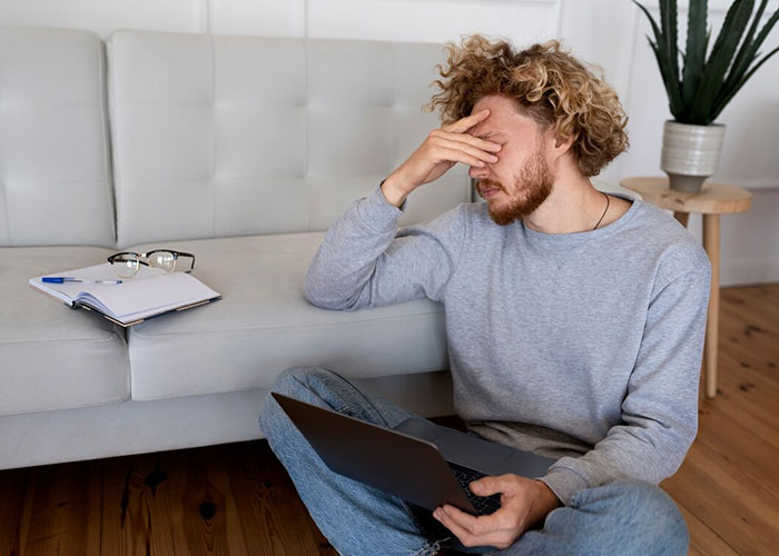 Man sitting by couch with laptop, looking concerned about missing from in-laws' anniversary collage. Man sitting by couch with laptop, looking concerned about missing from in-laws' anniversary collage.