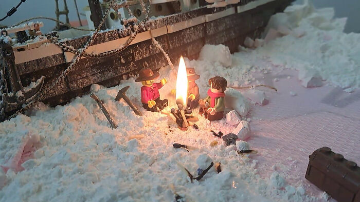 LEGO figures reenact the Imperial Trans-Antarctic Expedition, gathered around a campfire with shipwreck in snowy backdrop.