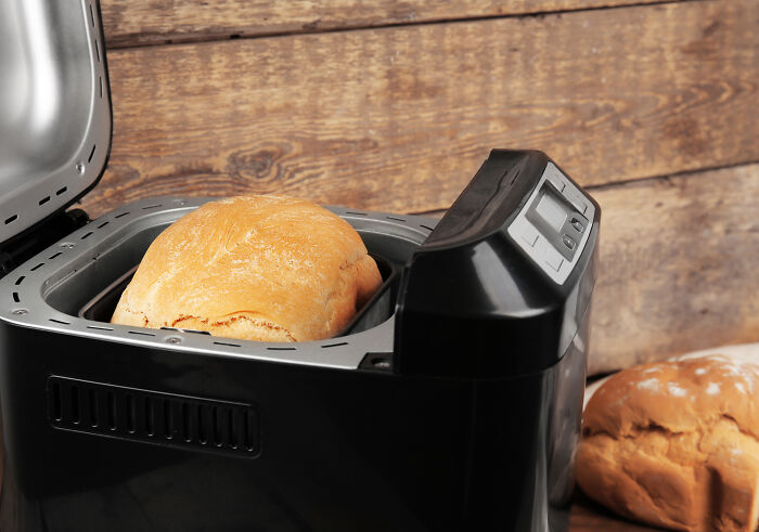 Affordable bread maker with fresh bread, open lid, and rustic wooden background.