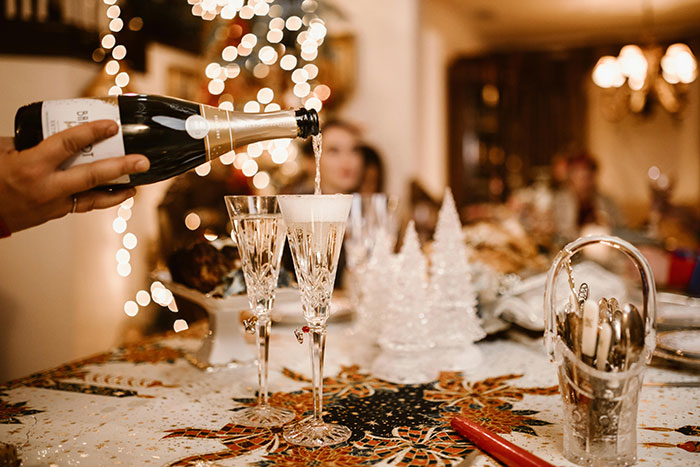Pouring champagne into crystal glasses on a festive table, with decorative lights in the background.