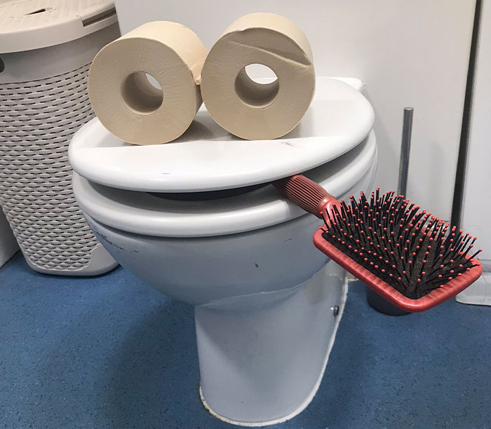 Toilet with two rolls and a brush arranged as a funny-wholesome anniversary surprise face.