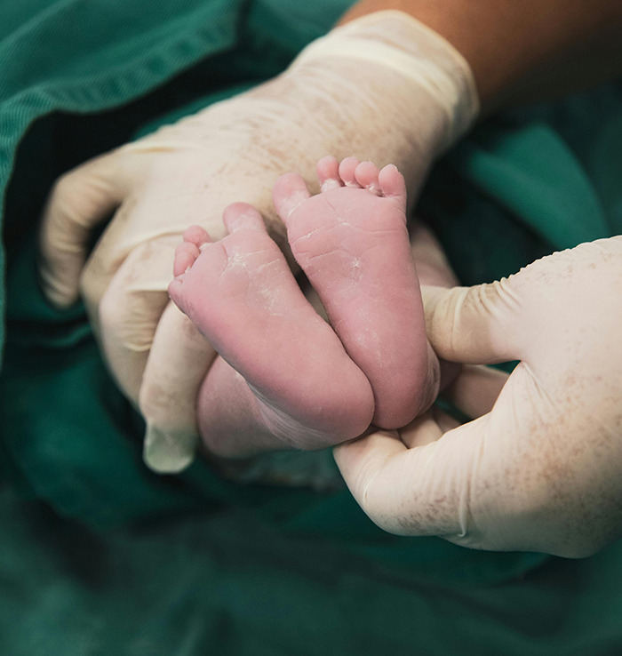 Newborn feet held by gloved hands in a hospital setting.