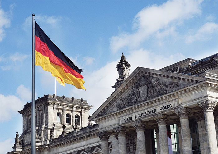 German flag waving outside the Reichstag building under a blue sky.