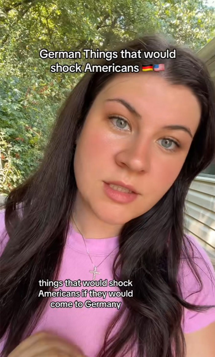 German woman in a pink shirt sharing cultural insights in a garden setting.