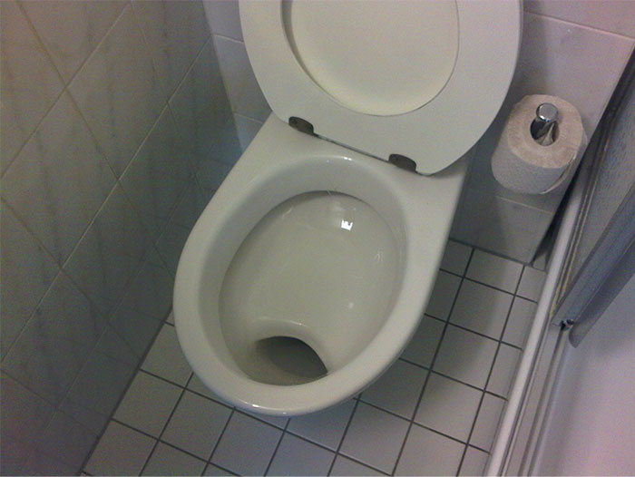 German cultural insight: a bathroom with a shelf toilet bowl and toilet paper on tiled floor.