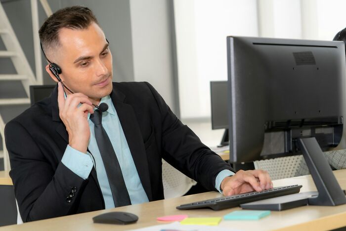 Man in suit at desk on headset, working remotely on high-paying job, using desktop computer.