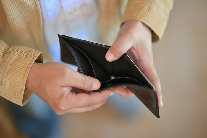 Man holding an empty wallet, focusing on financial struggles and judgment in society.