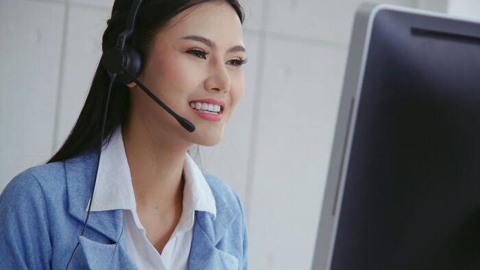 Woman in a headset smiling at a computer, illustrating high-paying remote jobs in a professional setting.
