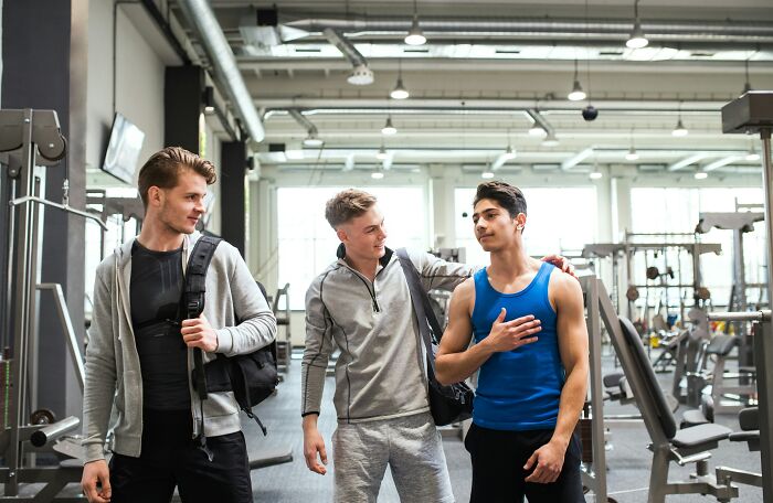 Three men in workout gear chatting in a gym, discussing space-saving gym accessories and equipment.