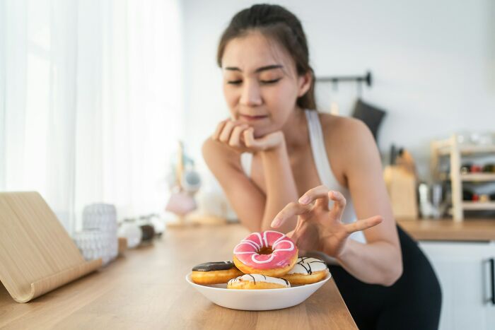 Woman reaching for a donut from a plate, possibly leading to weight gain.