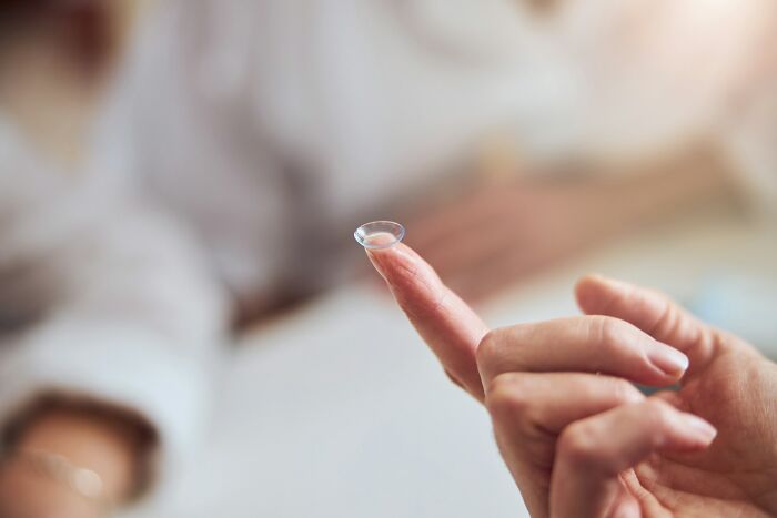 A person holding a contact lens on their fingertip, showcasing intriguing facts about vision and optics.