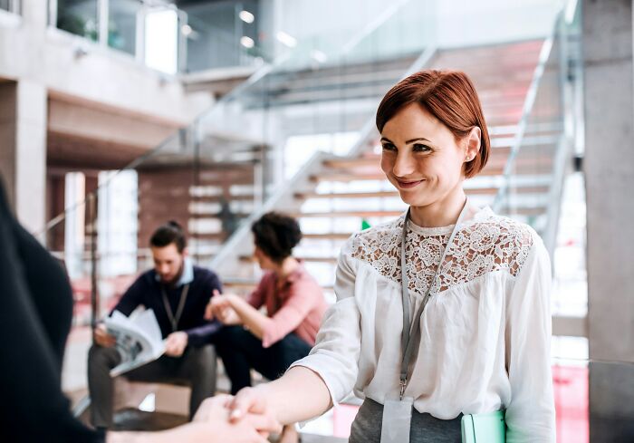 Woman smiling in a modern office setting, shaking hands, symbolizing high-paying remote jobs collaboration.