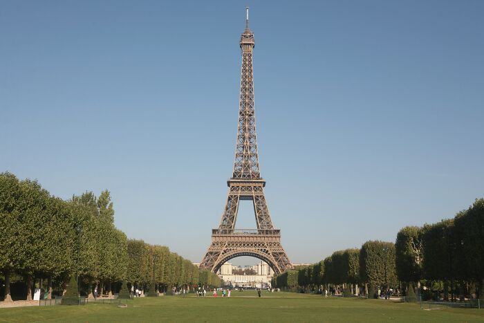 Eiffel Tower under a clear sky, surrounded by trees and a green lawn.