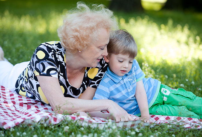 Grandma and child on a picnic blanket outdoors, enjoying a sunny day in the park.
