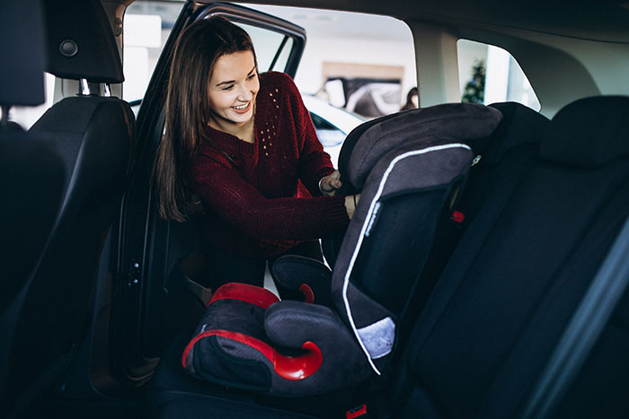 A woman places a car seat in the back of a vehicle, emphasizing child safety.