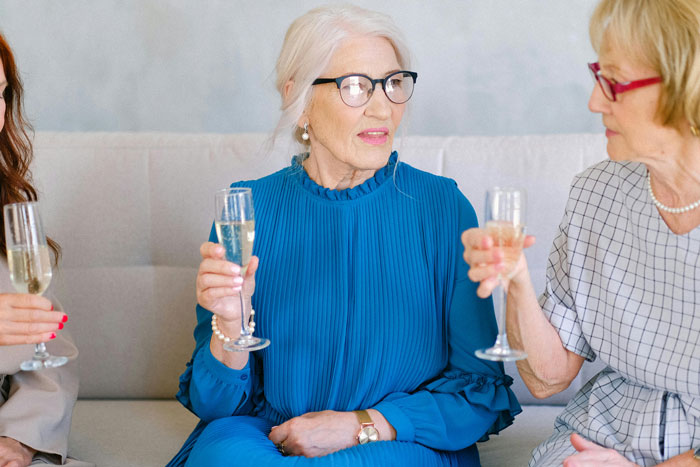 Elderly women at a rehearsal dinner, one in a blue dress, holding champagne.
