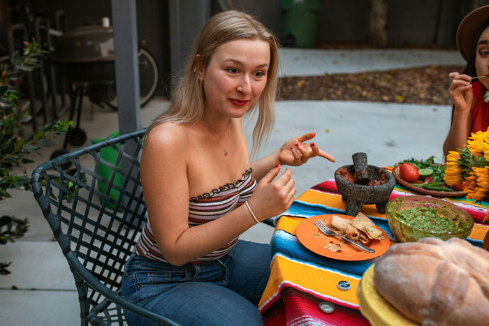 Woman at outdoor dinner, talking animatedly with food on a colorful table.