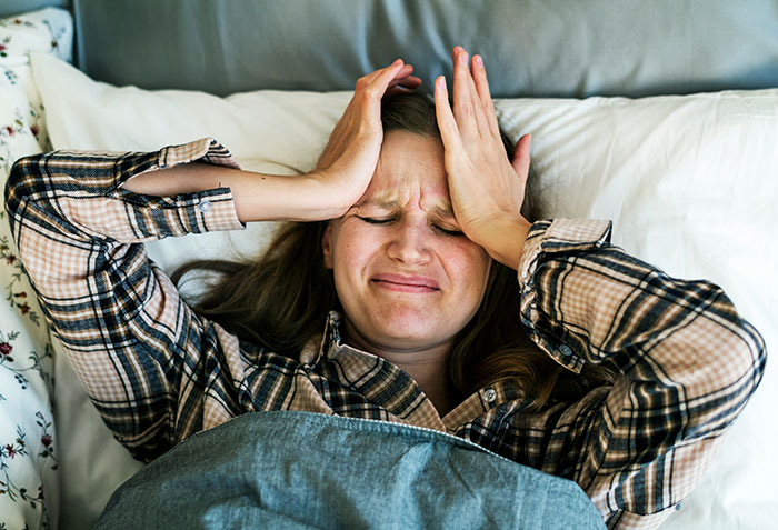 Woman in bed with a pained expression, holding her head.