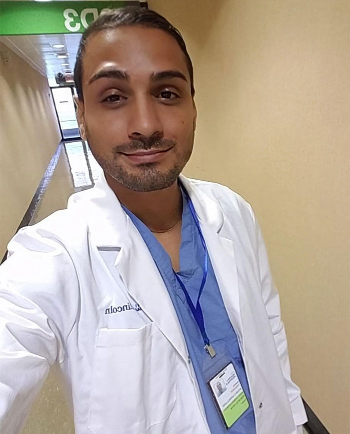 Man in a white coat with a blue scrubs and ID badge, symbolizing journey from homelessness to surgical assistant.