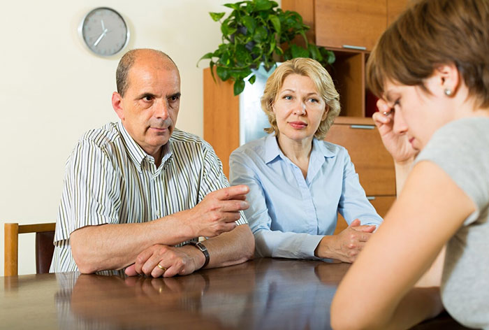Man and woman talking to a young woman at a table, related to stepmother's insults about weight.