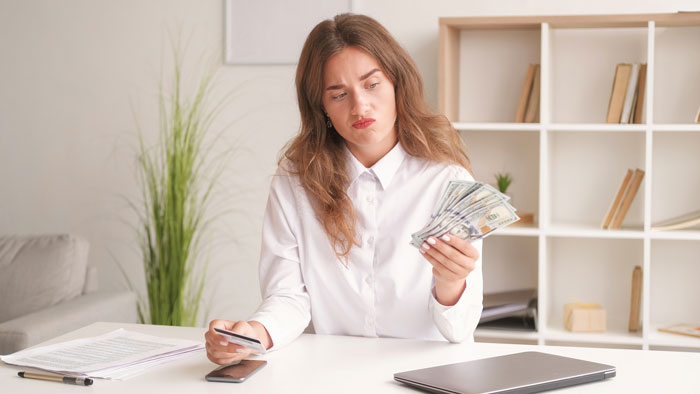 Woman at desk holding cash, concerned about hospital expenses for sister's childbirth.