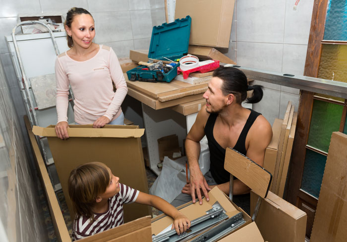 Woman, man, and child assembling furniture in a small room with tools and boxes, considering suing family over unpaid bill.