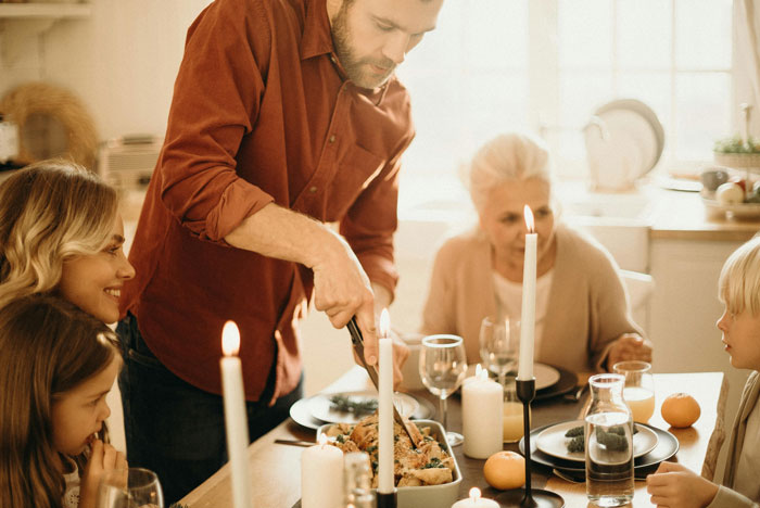 Husband serving food to family at dinner table, with wife and children, creating a warm cooking atmosphere.