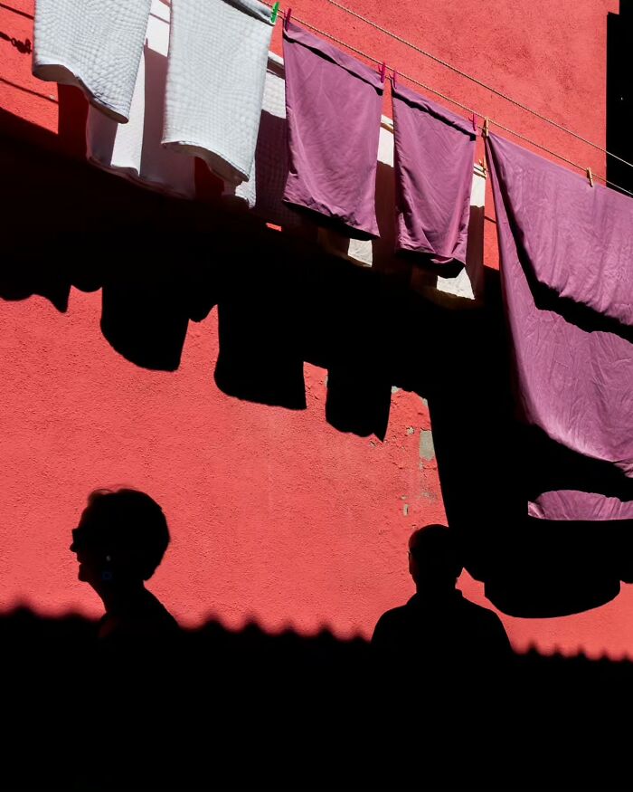 Silhouetted figures and laundry against a vibrant red wall, showcasing captivating street photography.