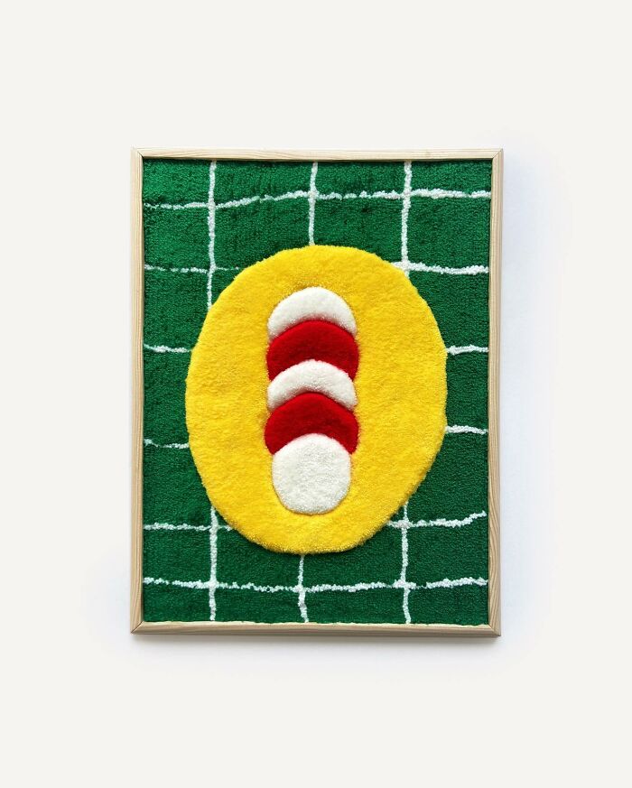 Tufted artwork by Cléa Delogu featuring geometric design with green, yellow, red, and white shapes in a wooden frame.