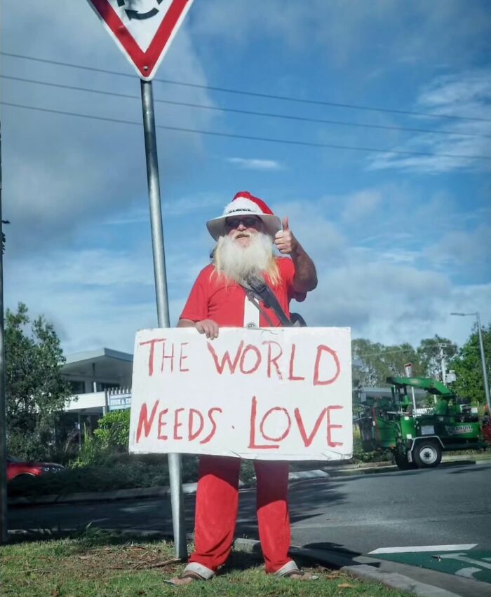 Santa-clad man in street, holding a sign reading "The World Needs Love," capturing pure street photography essence.