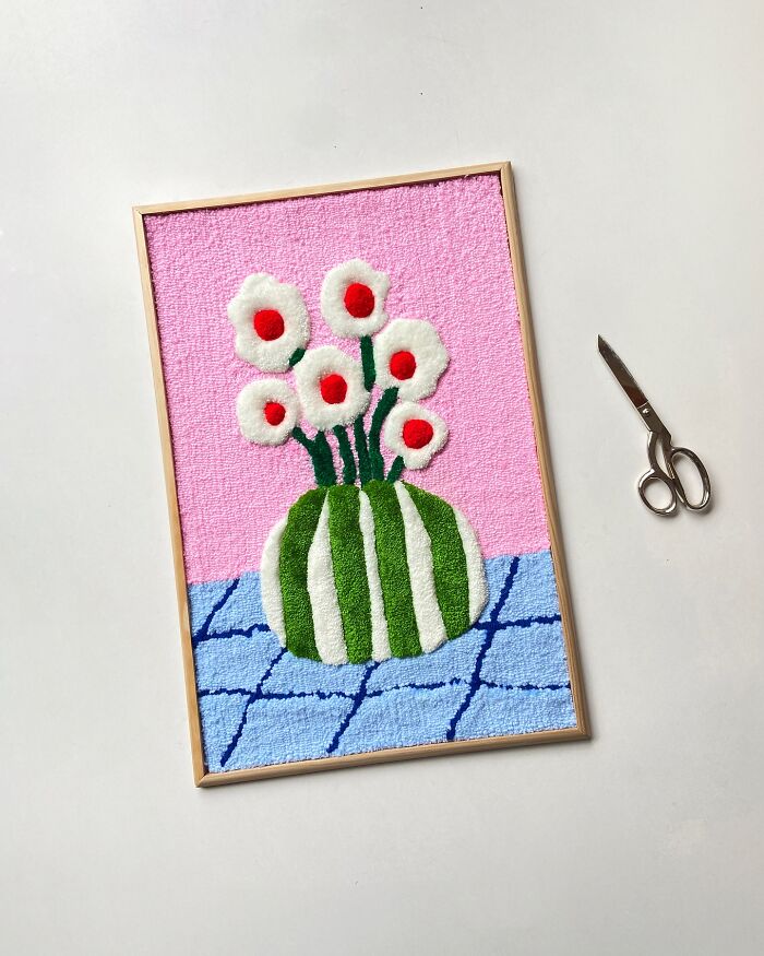 Tufted artwork by Cléa Delogu featuring abstract flowers in a green vase on a pink and blue background.