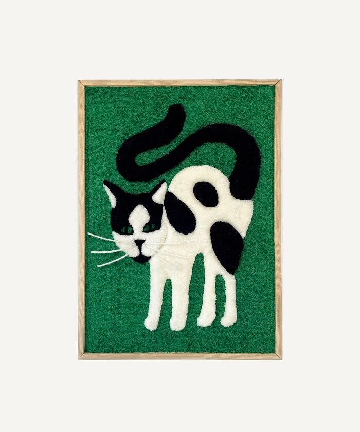 Tufted artwork depicting a black and white cat on a green background in a wooden frame.