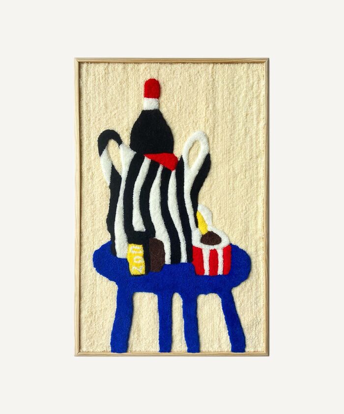 Tufted artwork with abstract shapes in red, blue, yellow, and black by Cléa Delogu, framed on a light background.