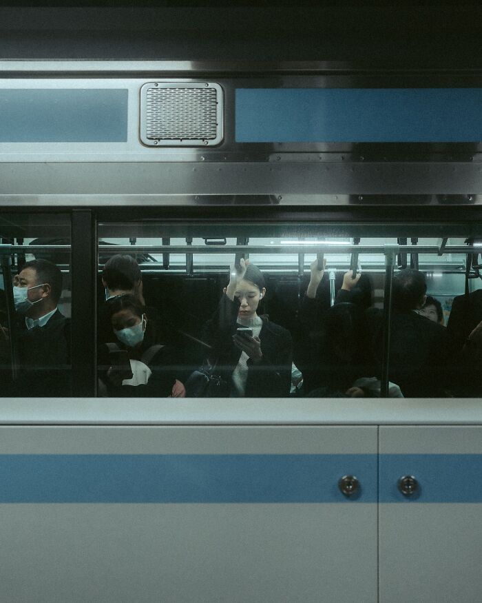 People inside a crowded train, engaging with their phones, capturing a street photography moment.