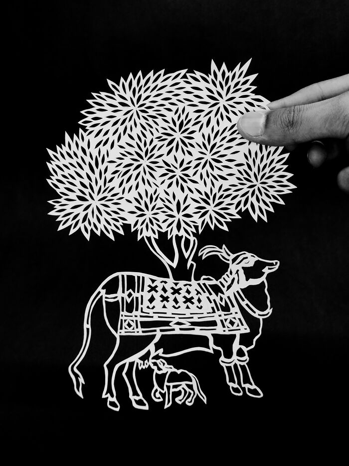 Paper-cutting art of a buffalo with calf under a tree, held by a hand, showcasing intricate detailing and craftsmanship.