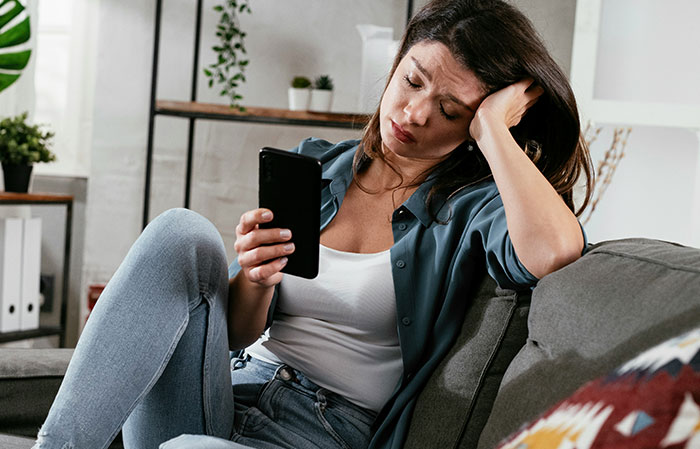 Woman looking frustrated on a couch while holding a phone, relating to unwillingness to babysit sister’s kids. Woman looking frustrated on a couch while holding a phone, relating to unwillingness to babysit sister’s kids.